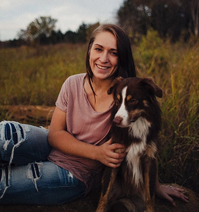 fiatal nő a mezőn ül a kutyájával